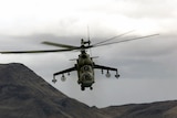 You view a helicopter travelling above a dark mountain range on an overcast day.