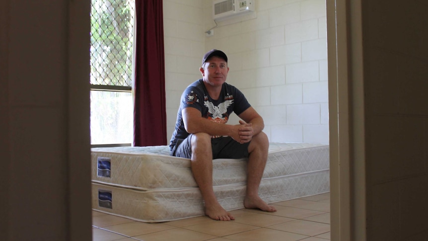 A man sits on a bed mattress in an empty room.