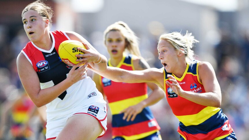 An AFLW forward marks the ball despite a despairing dive from a defender.