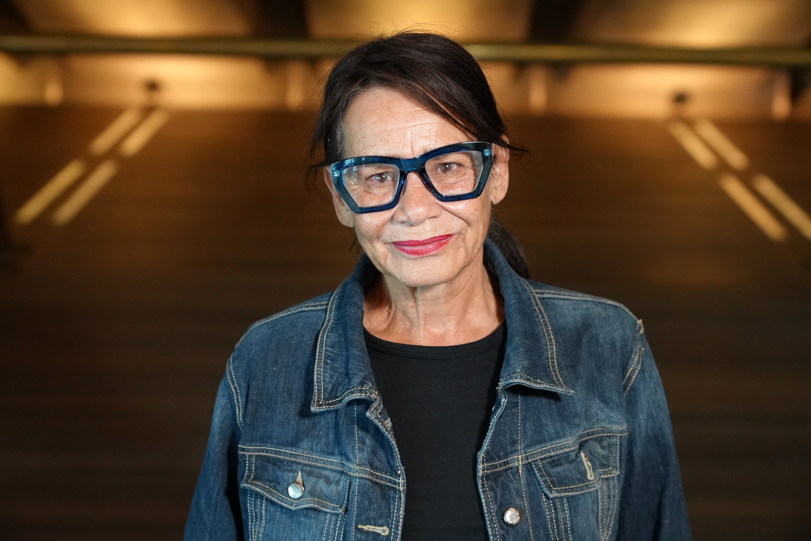 A photo of Rhoda, she is looking at the camera with glasses and hair pulled back. She is wearing a demin jacket