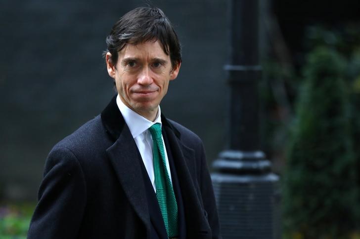 Rory Stewart smiles slightly as he looks to the right. He wears a dark overcoat and a suit with a green tie.