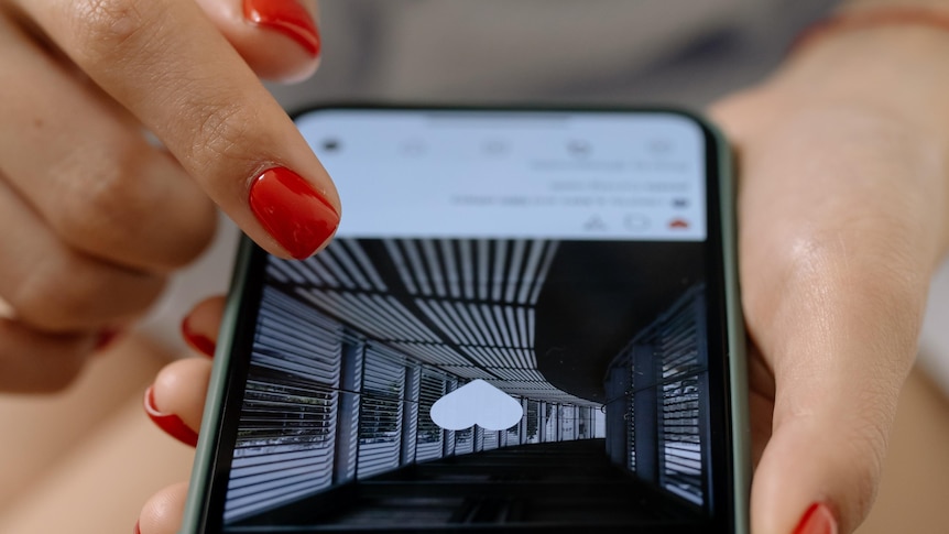 A photo shows a woman wearing red nail polish scrolling through a social media app on her phone