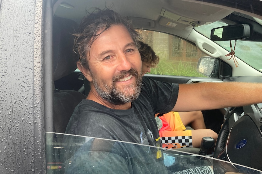 Un homme au volant de son véhicule, souriant.