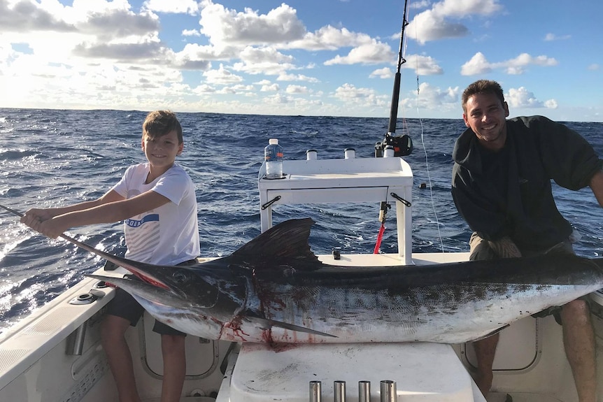 Two people on a boat display a marlin they have caught.