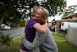 Woman in purple shirt hugging woman in grey jumper on street