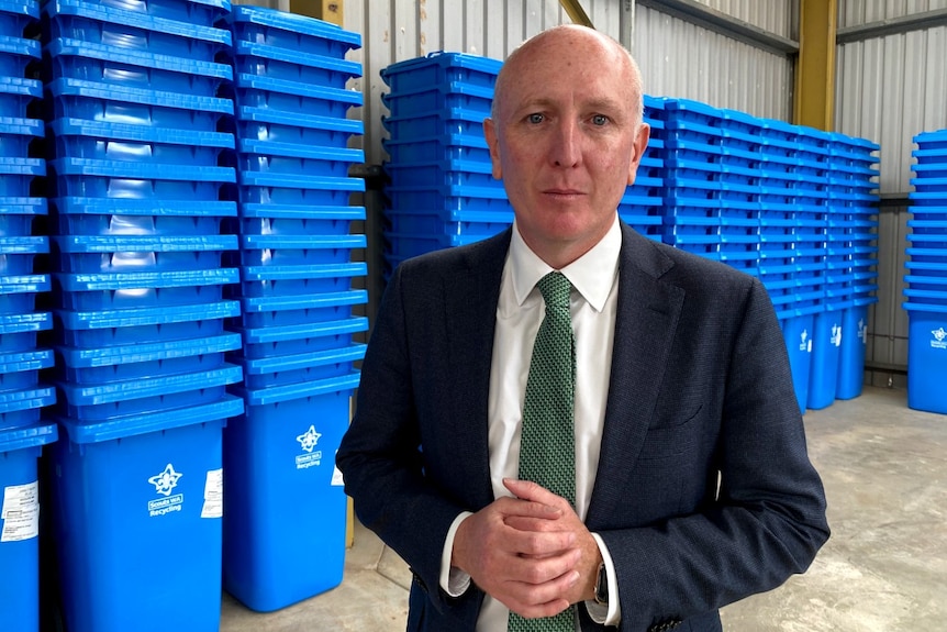 A man wearing a suit stands in front of piles of bright blue plastic crates.