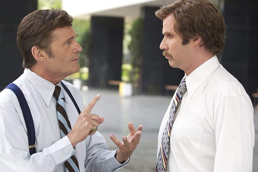 a man in a tie and white shirt talks to a man with a tie and white shirt and moustache