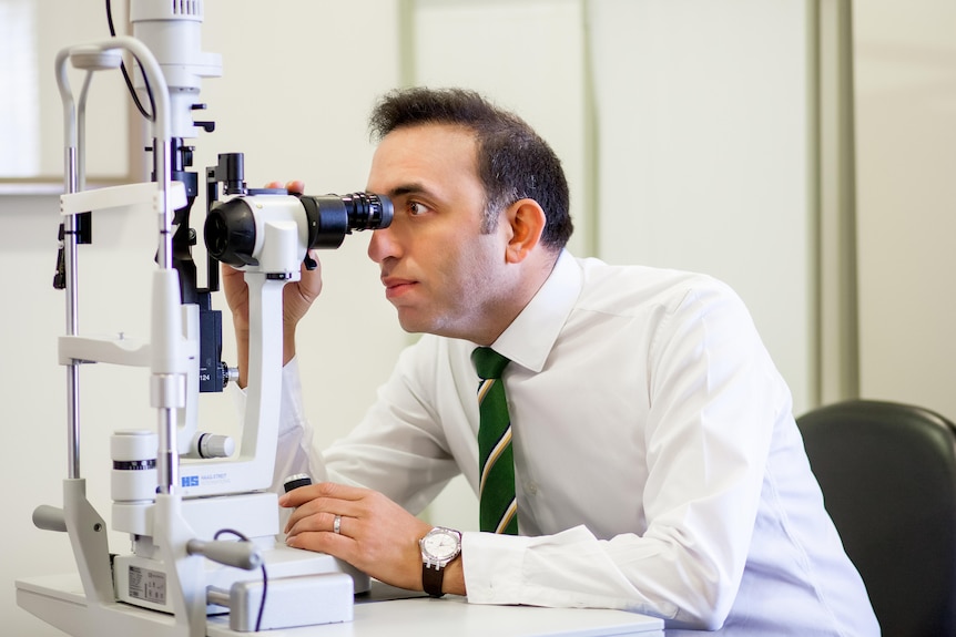 Dr Ezra looks through a microscope in an office.