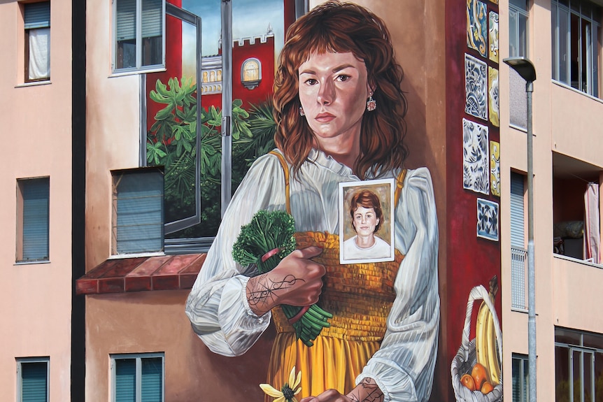 A large portrait of the artist painted on the side of an appartment building. It pictures the artist gazing out at the viewer