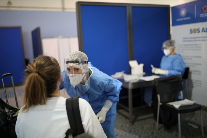 A woman in PPE looking at a woman in an airport