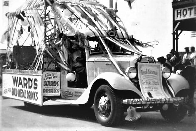A historic photo showing a delivery truck with streamers and other paraphernalia on it, part of a float in a parade 