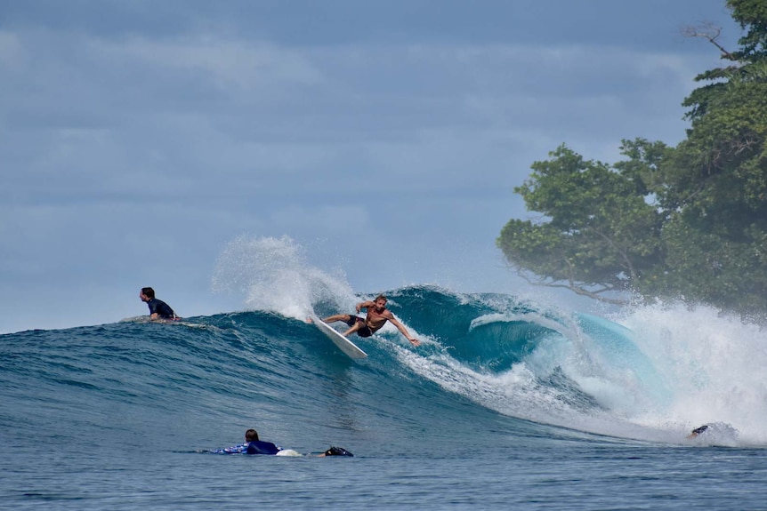 A surfer catches a wave in a promotional image by Banyak Surf Resort.