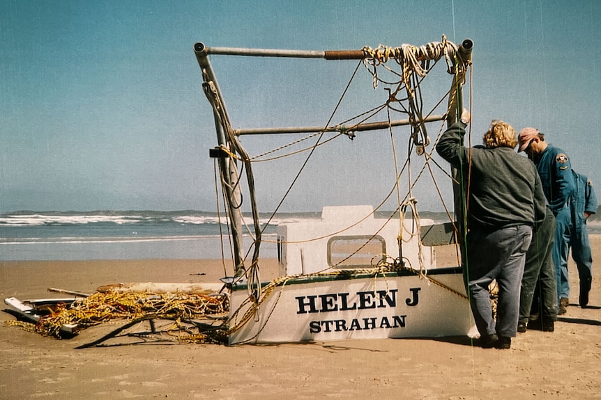 A crayboat sits wrecked on the beach with policemen and others looking it over.