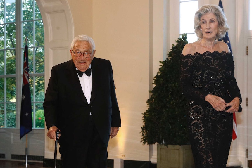 Henry Kissinger walks with a cane into the state dinner at the White House alongside Nancy Kissinger.