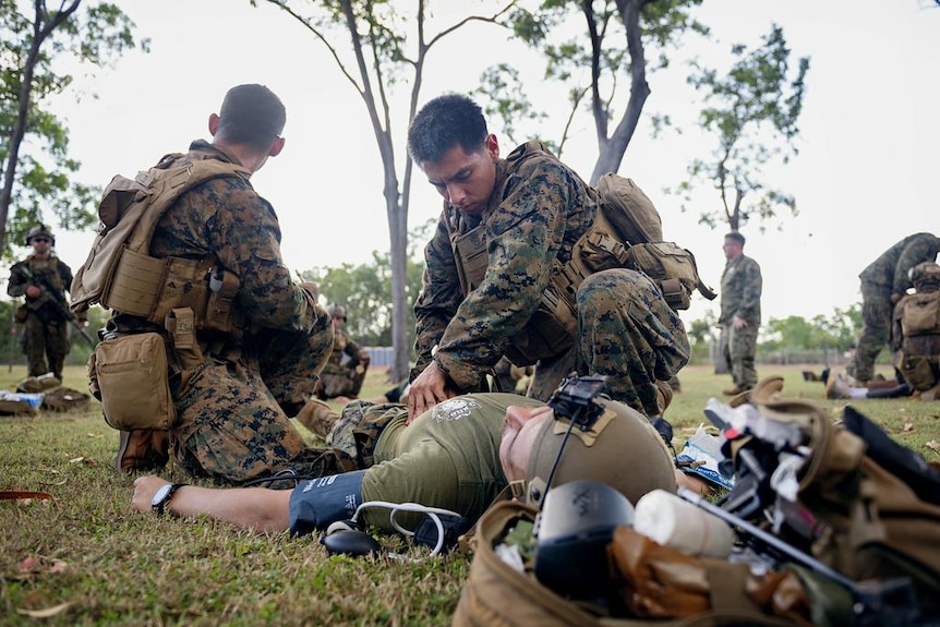 Two marines kneeling over a person on the ground, providing first aid