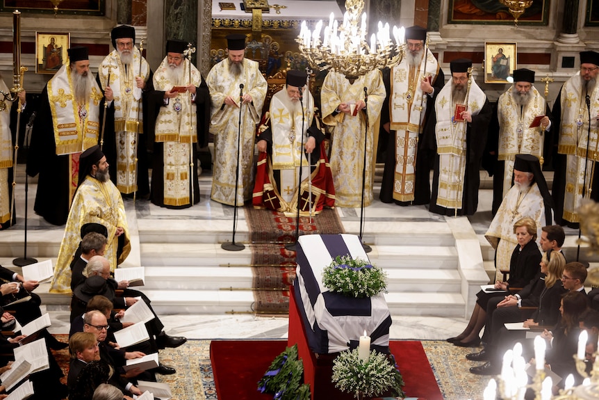 An image from inside a cathedral where the funeral ceremony took place. In the middle stands a coffin draped with a Greek flag