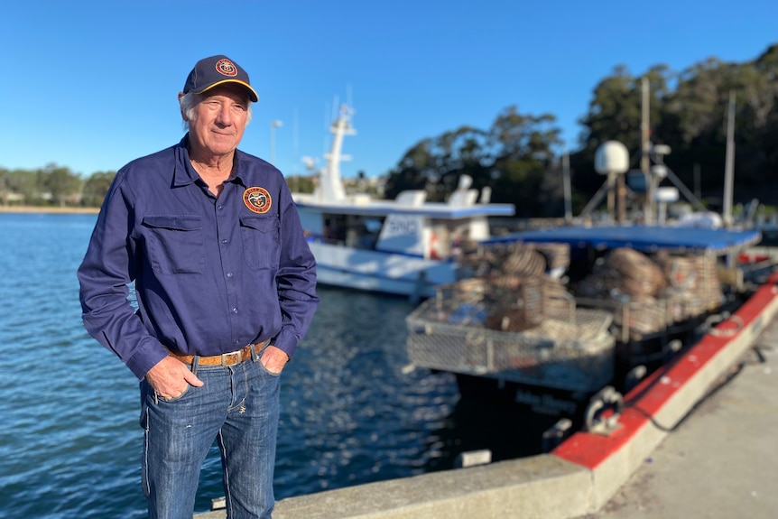 John smiles at the camera while standing in front of boats on the water.