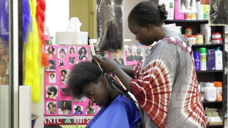 Woman stands, doing the hair of another woman, seated