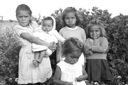 A black and white photo of five Indigenous girls posing for the camera in a field of flowers.