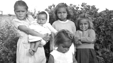 A black and white photo of five indigenous girls posing for the camera in a field of flowers.