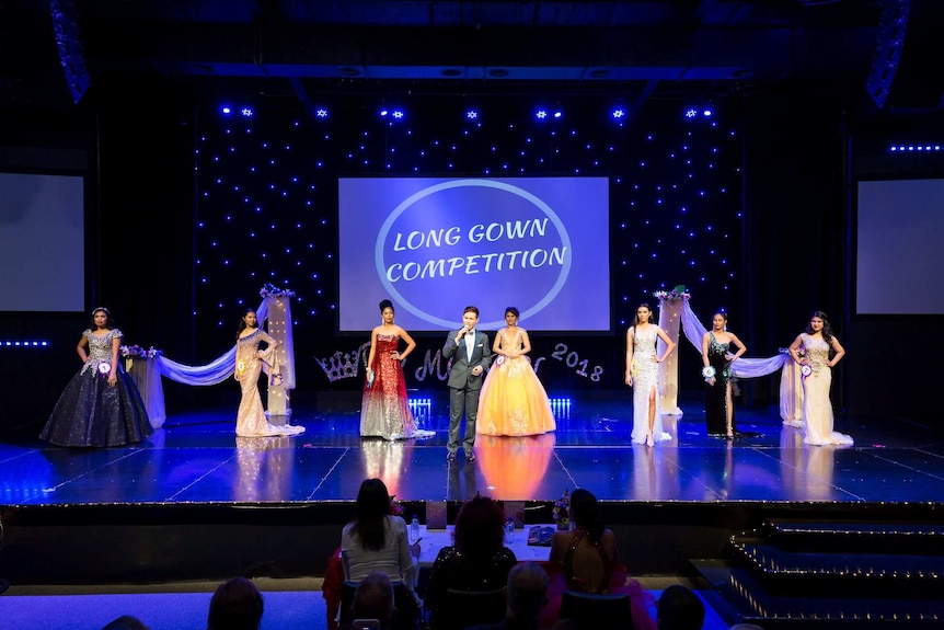Ladies in long gowns stand on a stage