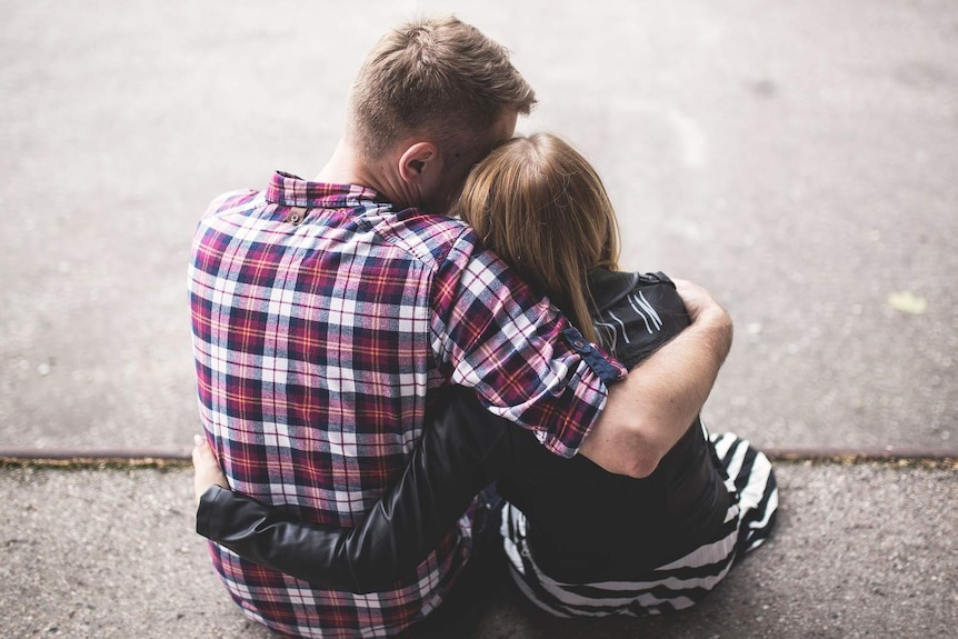 Man and woman sitting on ground and hugging each other for a story about helping someone out of an abusive relationship.
