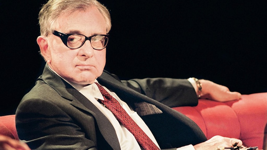 A man in glasses and a suit sits on a red couch