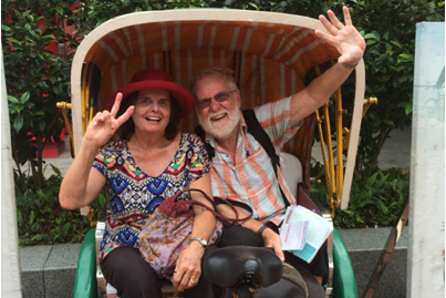 A woman making a peace sign and a man waving sit in a carriage smiling.
