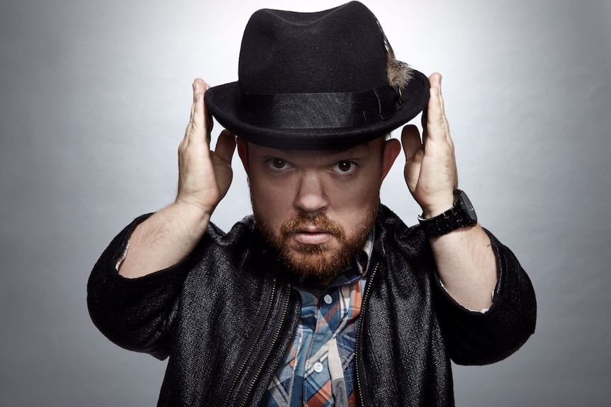 A professional headshot of comedian Brad Williams he is wearing a hat.