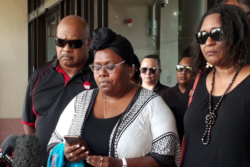 A woman looks at her phone surrounded by family members.