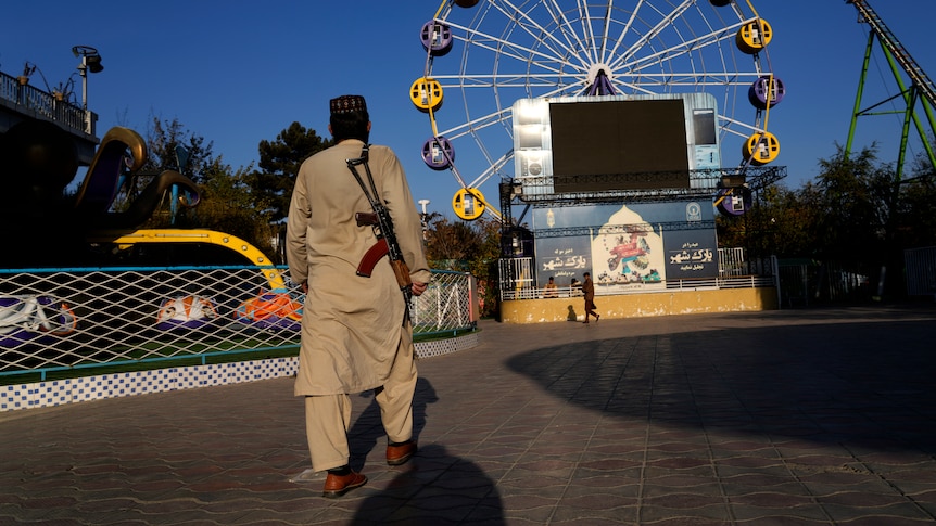 An armed Taliban fighter in Khaki dress stands guard in an amusement park.