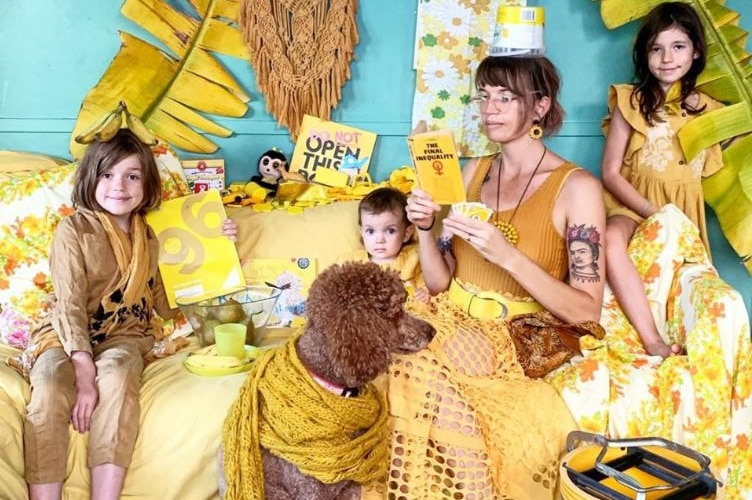 Three children, a woman and a dog wearing yellow sit in a loungeroom surrounded by objects that are also yellow.