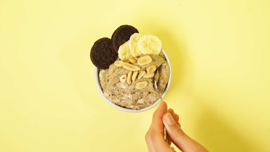 Banana nice cream in a bowl topped with chocolate cookies, peanuts and banana slices.