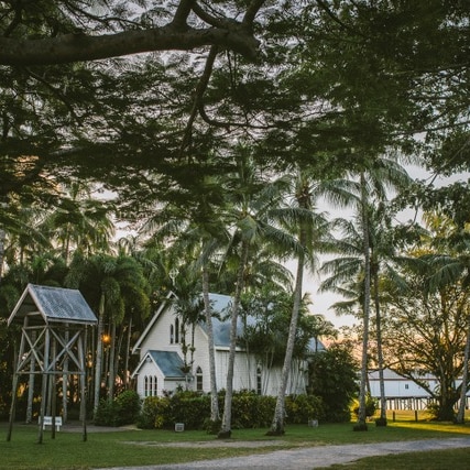 A small white church in front of the sea, surrounded by palm trees.