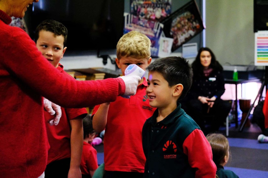 Students line up to have their temperature checked. A woman points a device at a students forehead.