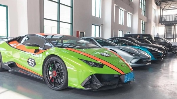 A row of high-end luxury cars, some with bright racing stlye painjobs, are parked in a cavernous garage.
