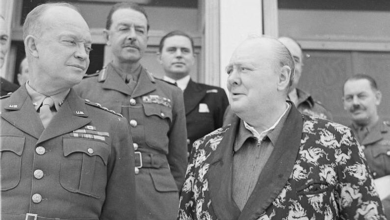 A man in a dressing gown stands beside a uniformed general and other men in uniforms in a black and white photo