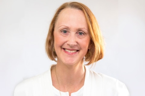 A headshot of a woman with strawberry blonde hair wearing a white jacket