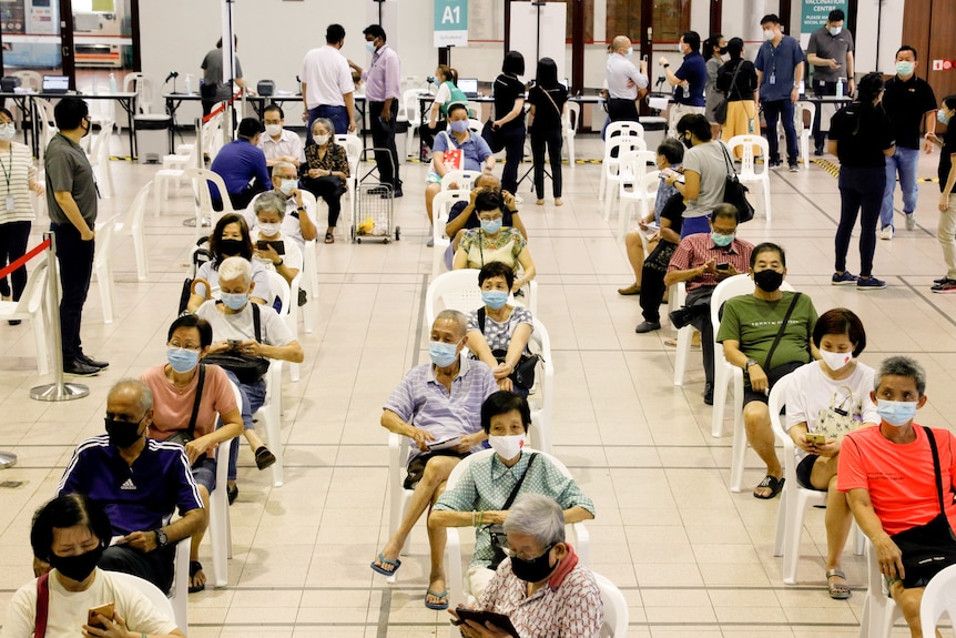 People aged over 70 wearing masks sit spread out in chairs.