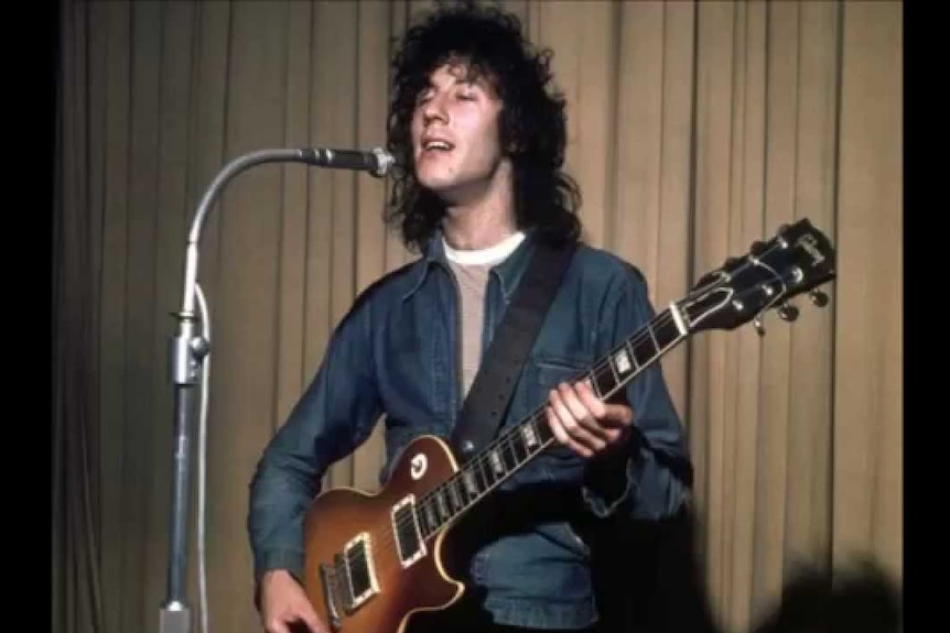 Peter Green holds a guitar and sings into a microphone.