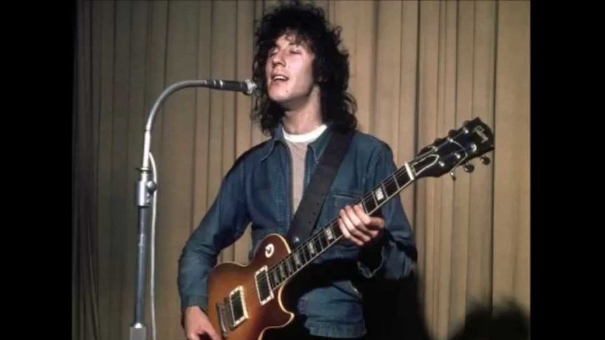 Peter Green holds a guitar and sings into a microphone.