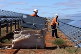 Two workers unpack solar panels from a large crate and place them onto a solar array frame