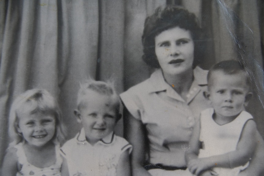 A black and white family portrait of a mother and three young children