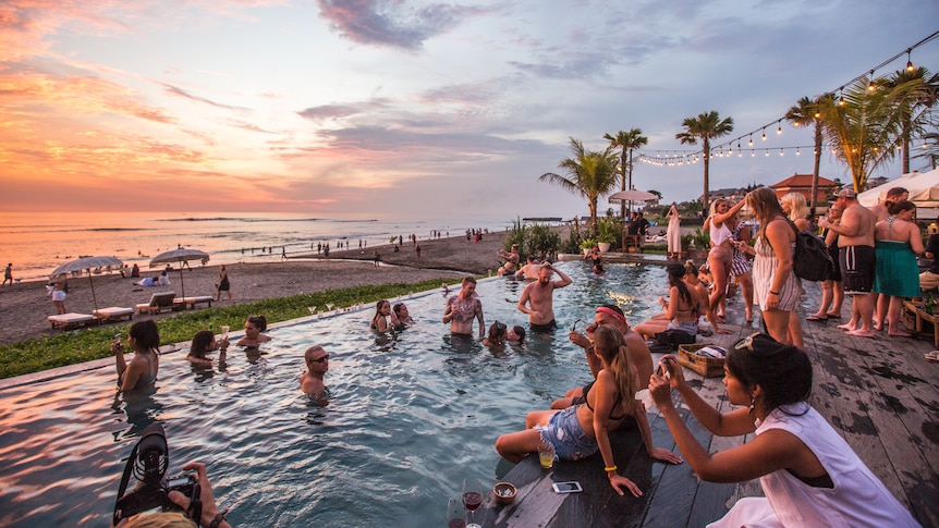 A pool full of people drinking near a beach during sunset. 