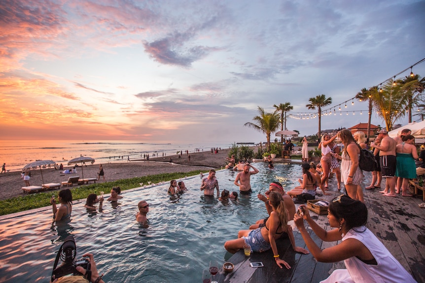 A pool full of people drinking near a beach during sunset. 