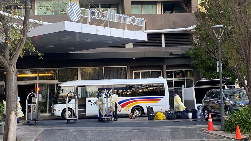 A small bus outside a hotel with people wearing PPE