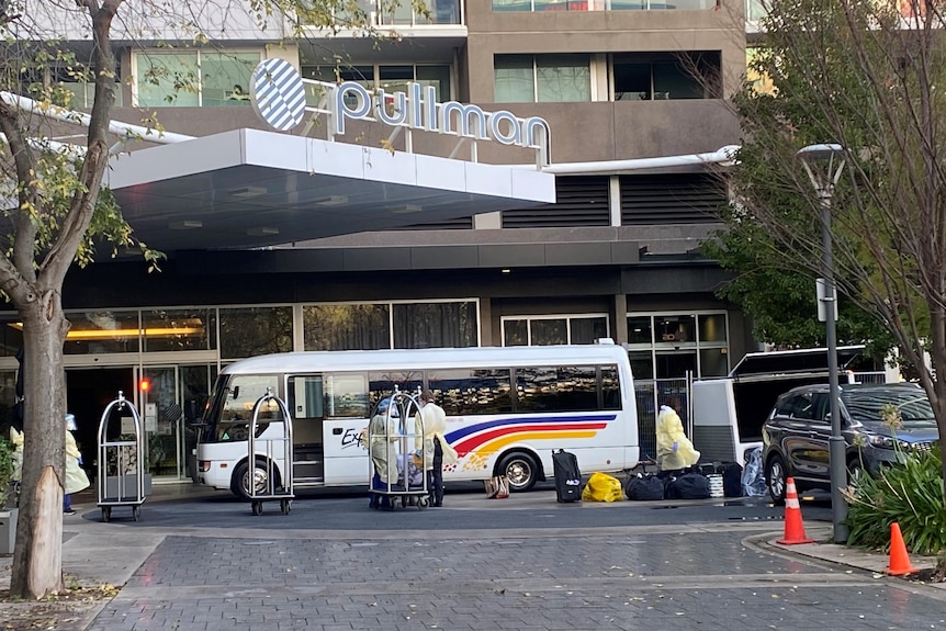 A small bus outside a hotel with people wearing PPE