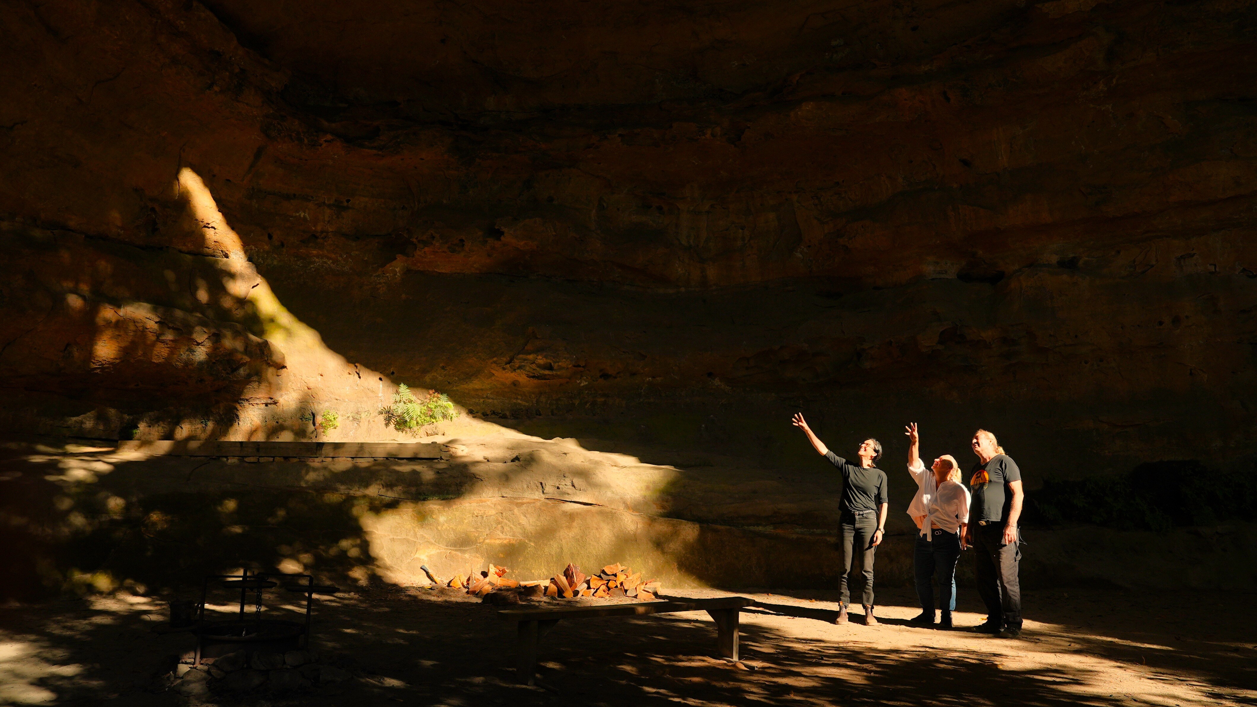 Three people stand inside a large cave.