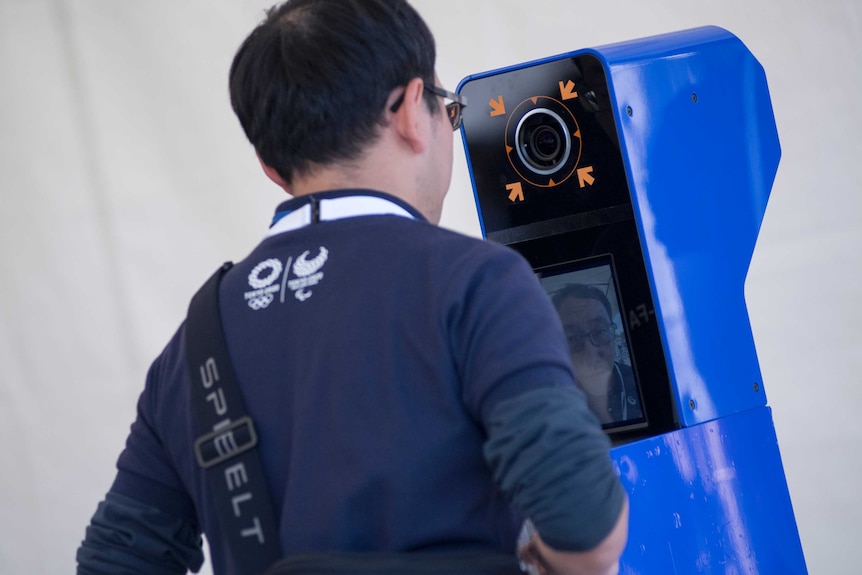 Man stands in front of a blue box which has a camera and screen.