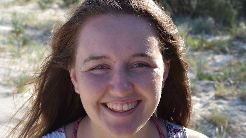 Young woman with brown hair smiling with sand dunes in the background